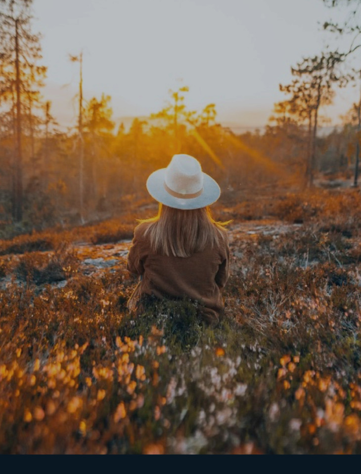 A woman sitting in a golden autumn field near Rovaniemi at sunset